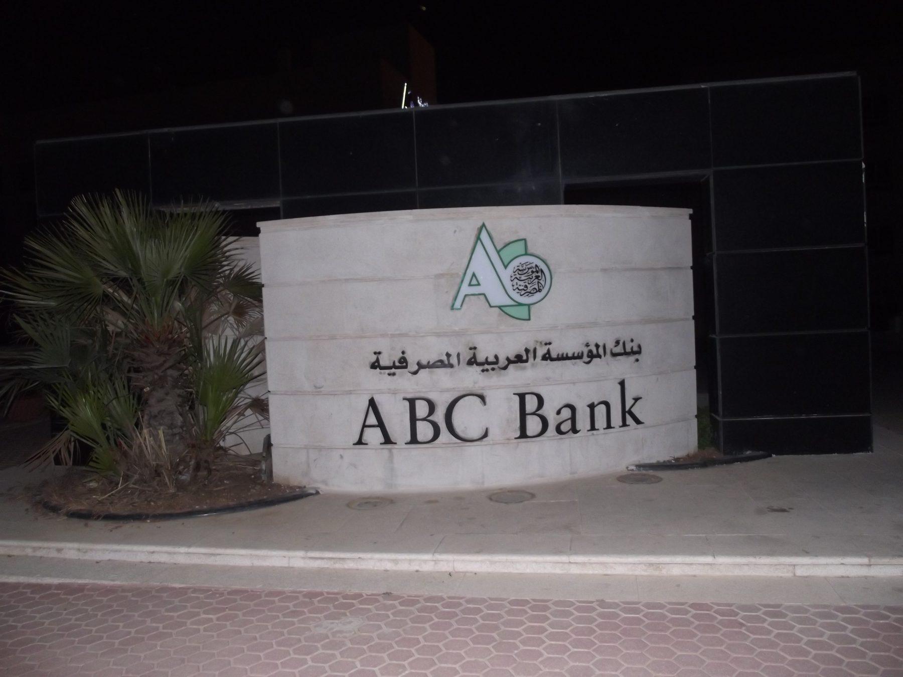 Curved stone-clad monument sign with logo and bank name, photographed at night.