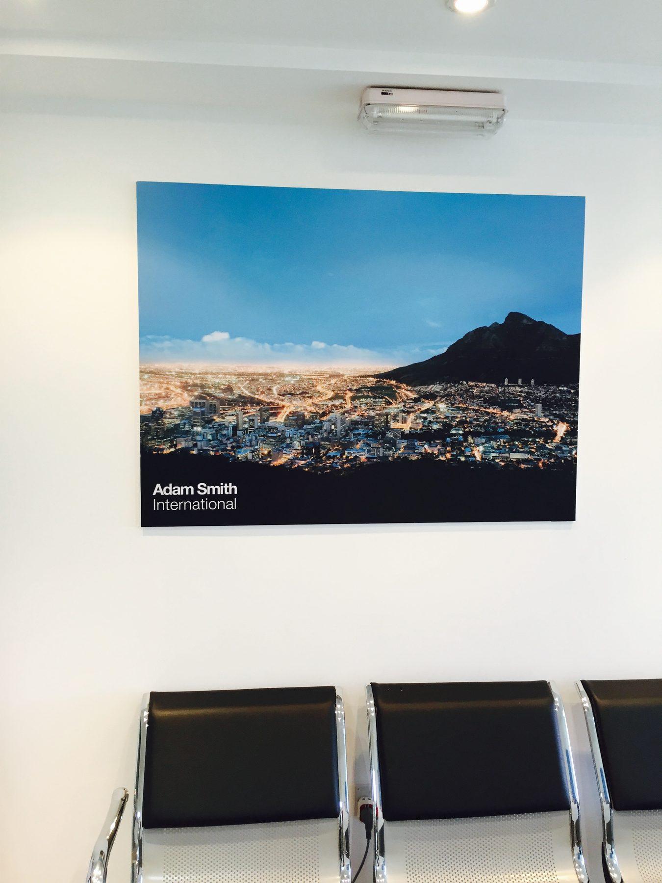 Printed photo panel of a city at dusk, hung above waiting chairs.