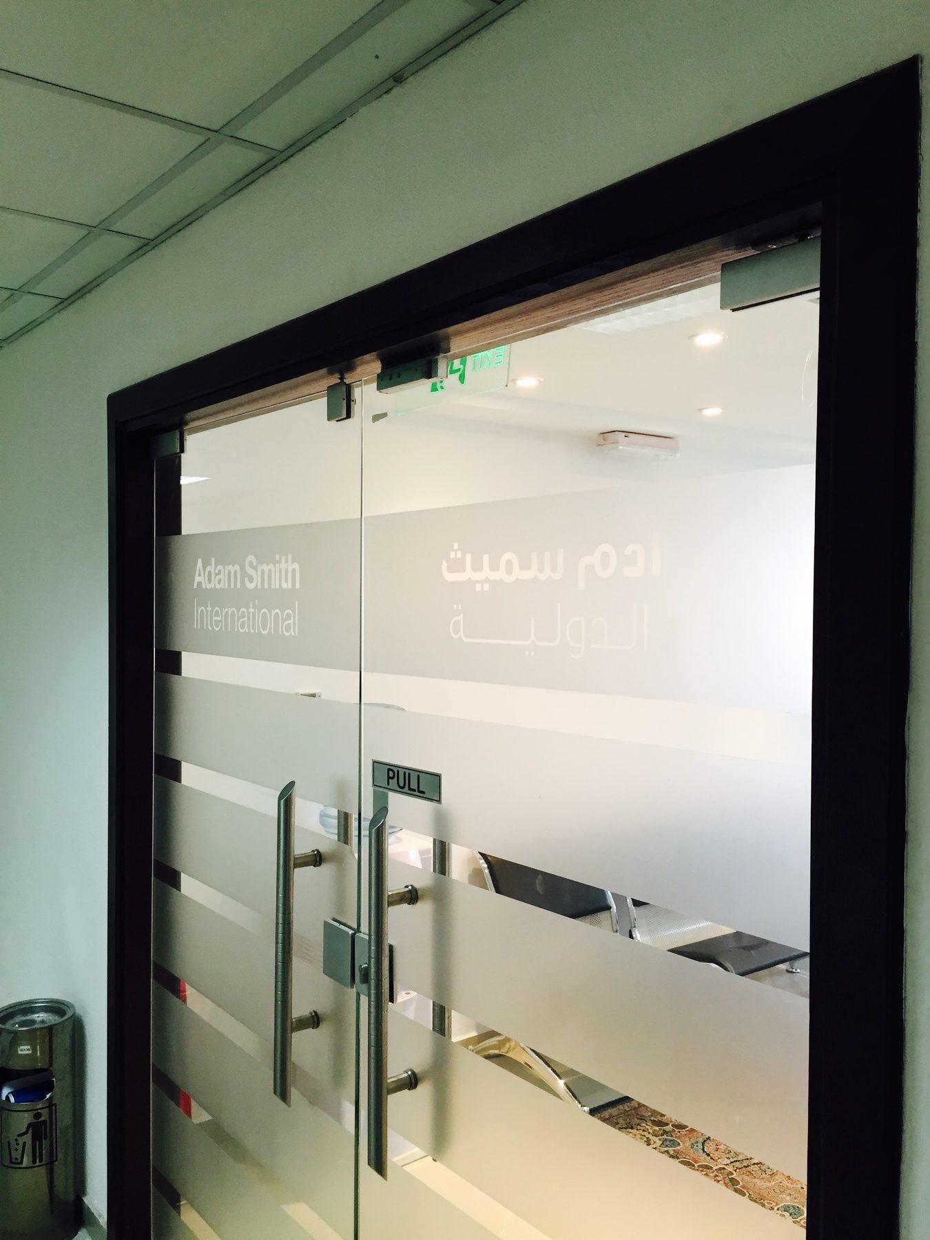 Frosted window film with the company name in English and Arabic on a glass door.