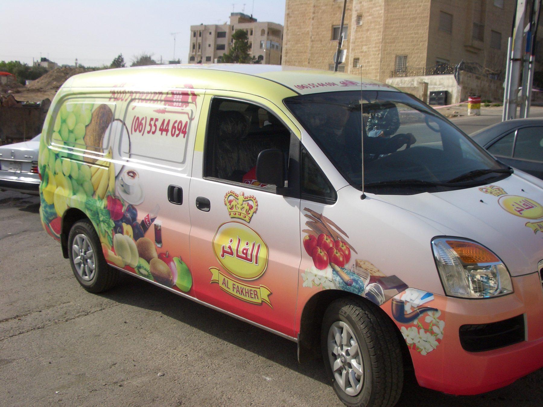 White van with a fruit-pattern wrap, brand crest and phone number on its side.