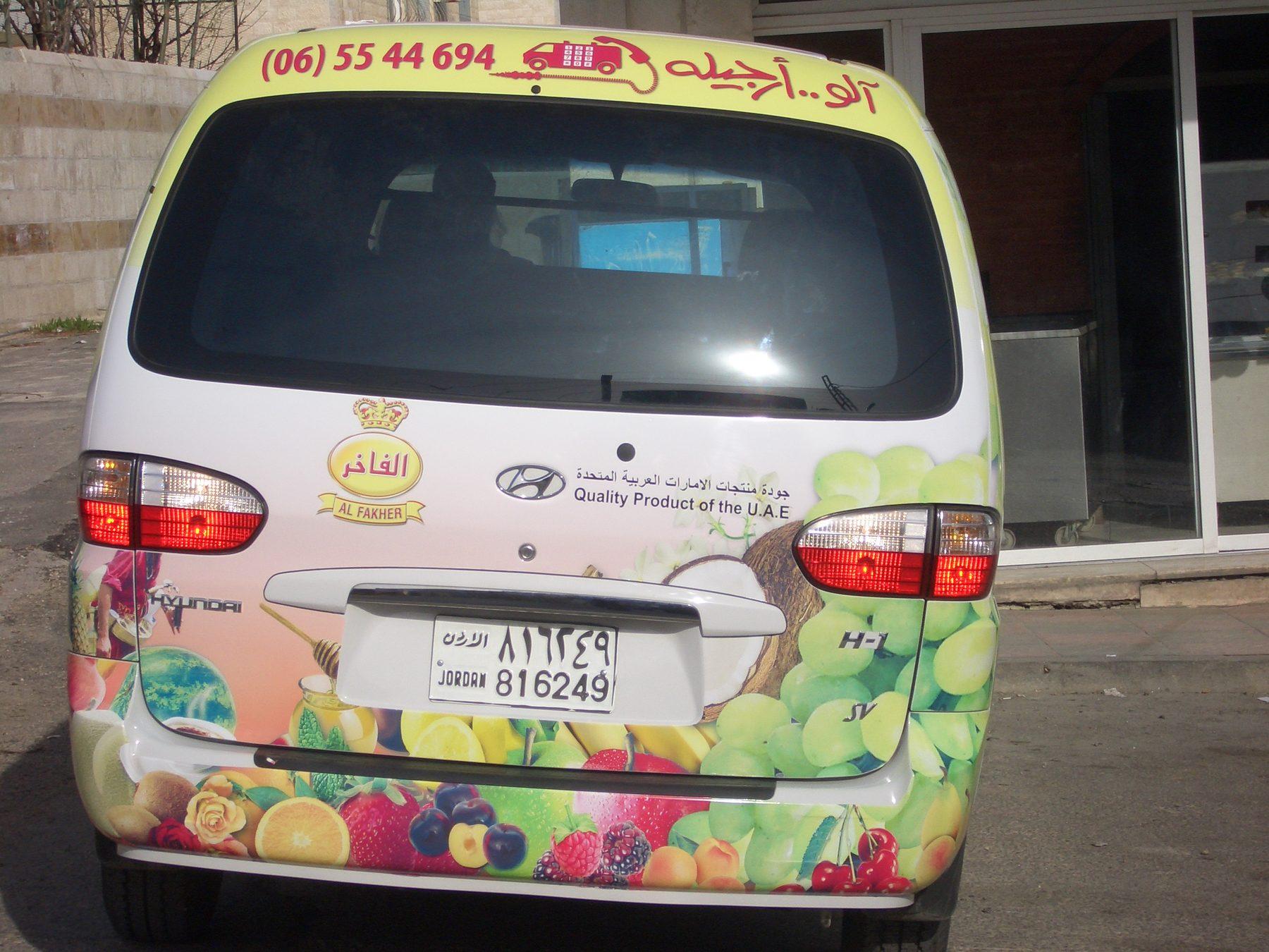 Rear of a white van with a fruit-pattern wrap and phone number on the tailgate.