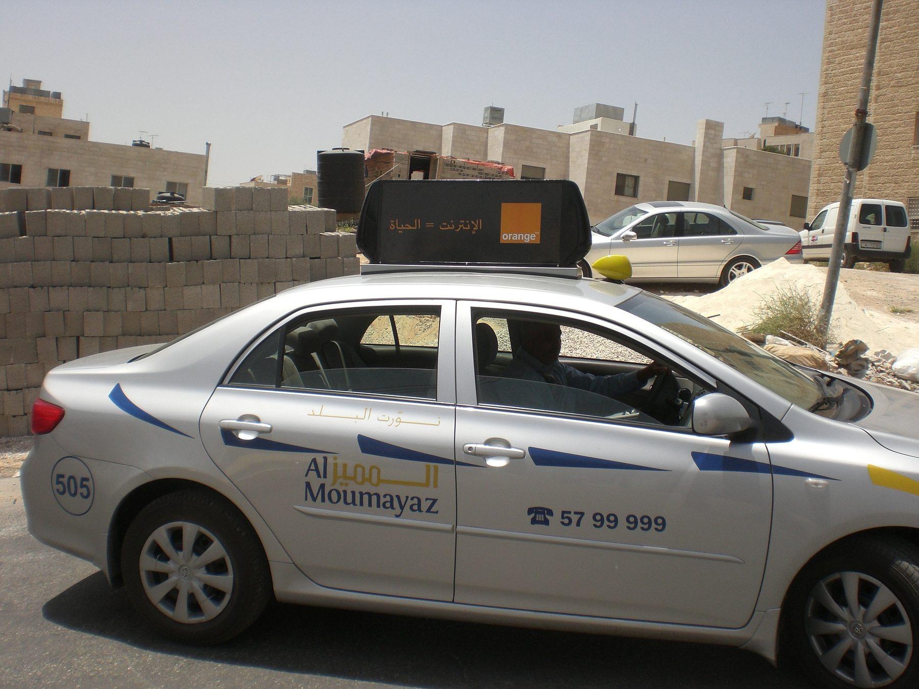 Silver taxi with lettering, phone number and roof sign