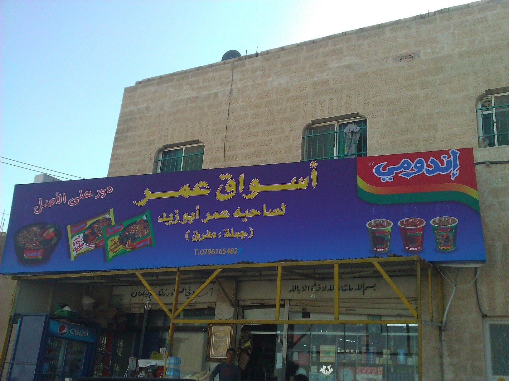 Blue printed fascia with Arabic lettering above a shopfront and stone facade