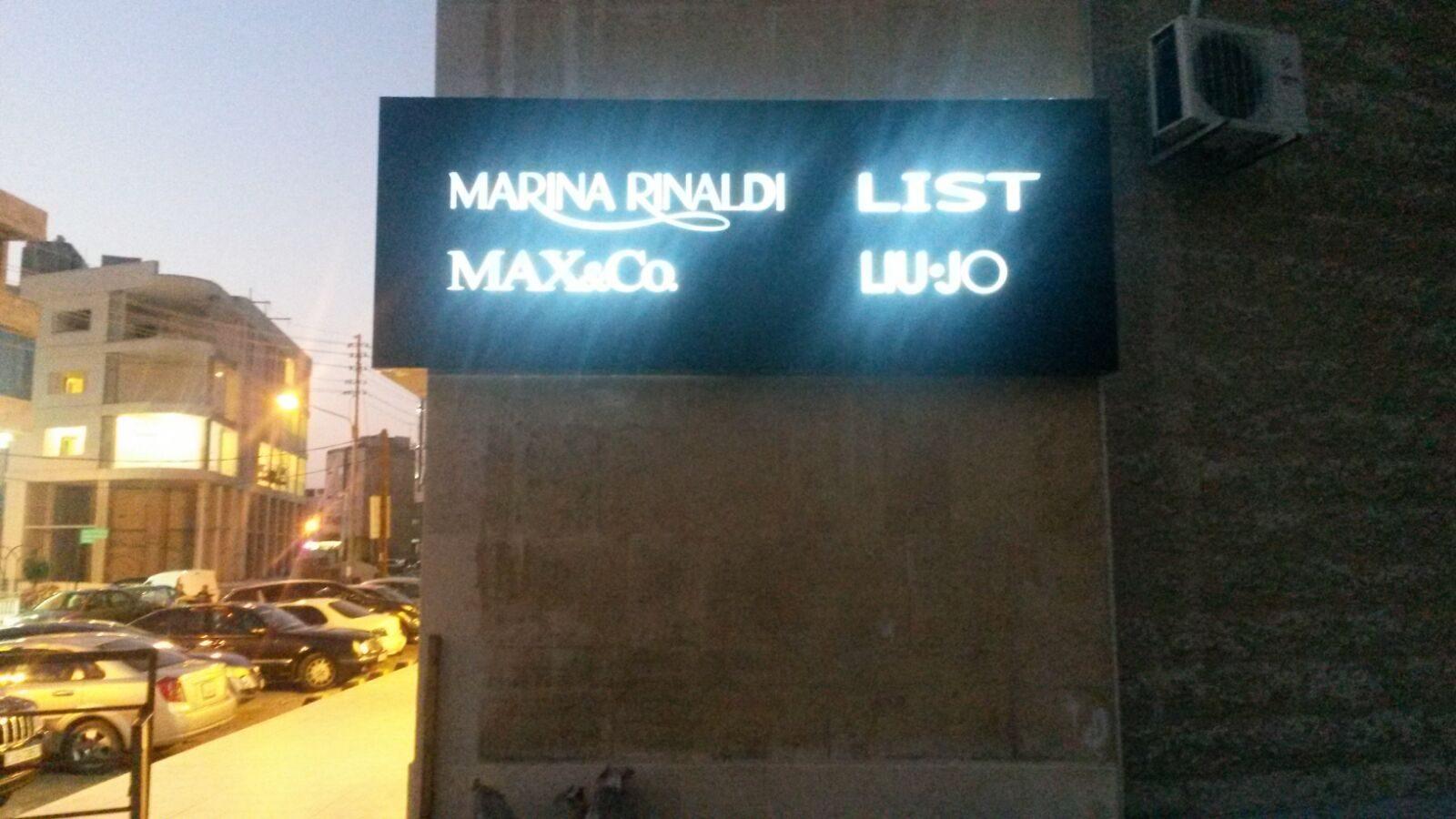Illuminated multi-name channel letters on a dark panel at dusk