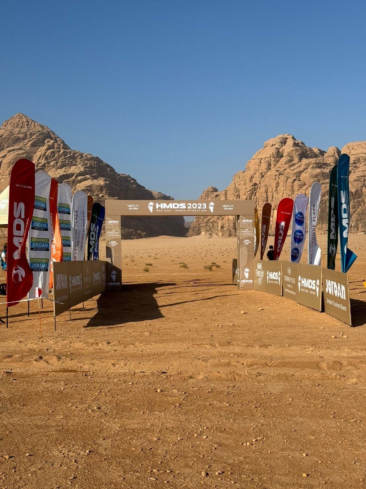 An event entrance arch flanked by flag banners in a desert setting.
