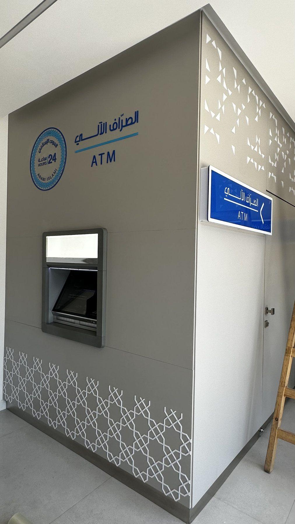 An ATM sign with a wayfinding plaque on a grey wall with a perforated pattern.