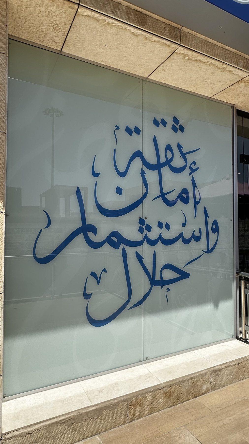 Frosted glass panel with blue Arabic calligraphy applied as a window graphic.