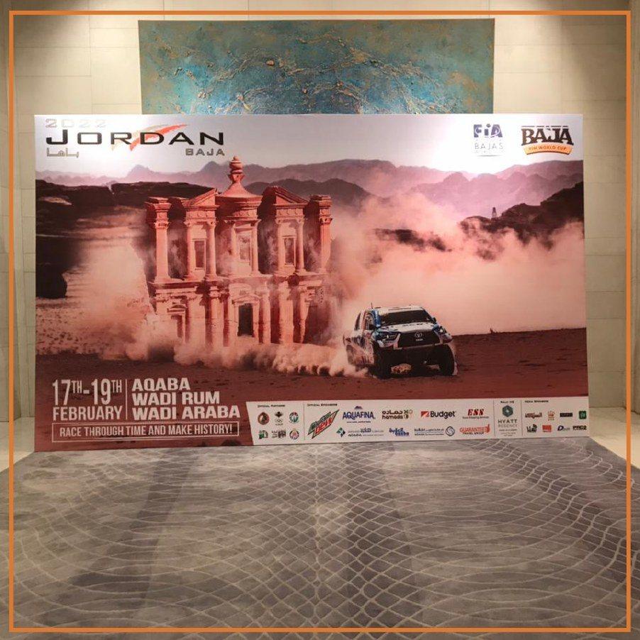 A printed event backdrop with a desert landmark image and sponsor logos.