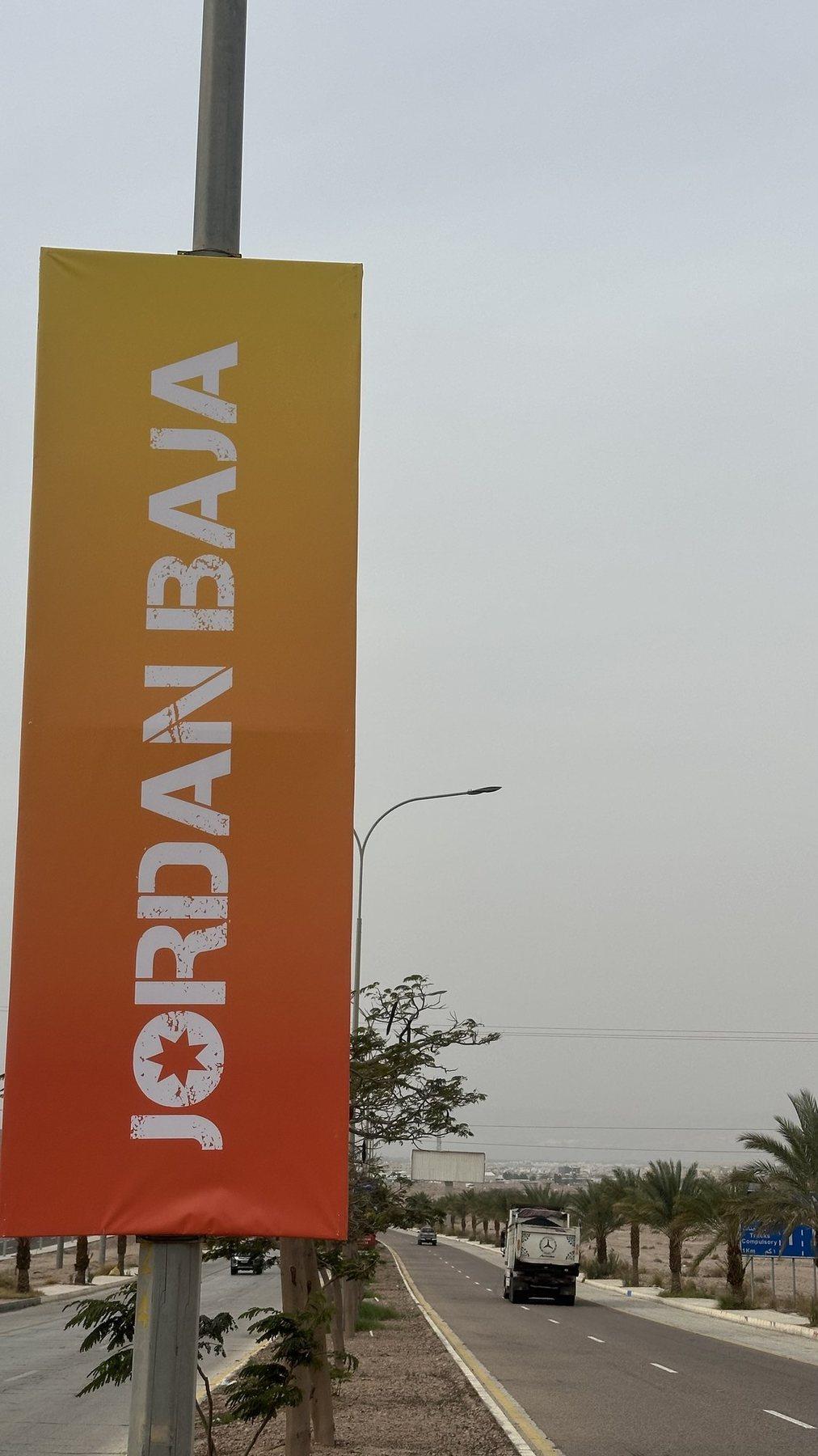 An orange vertical banner hangs on a street lamp pole beside a road.