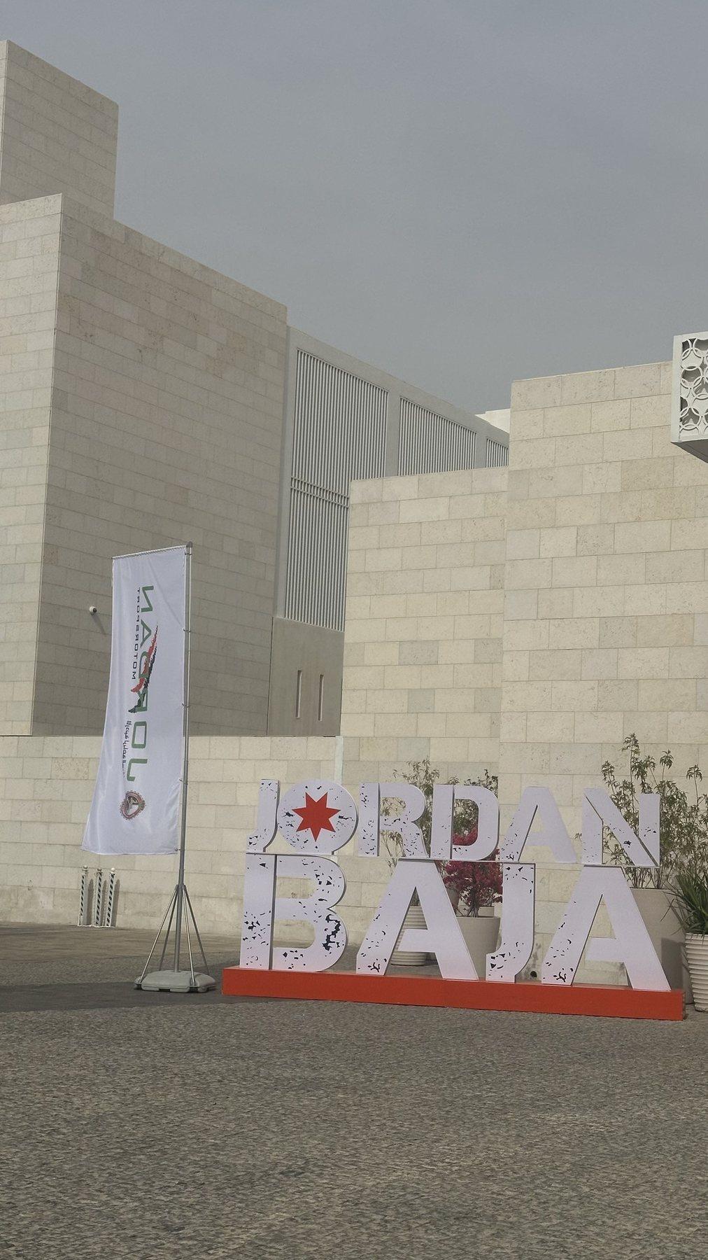 Large red and white lettering stands outside a building with a flag nearby.
