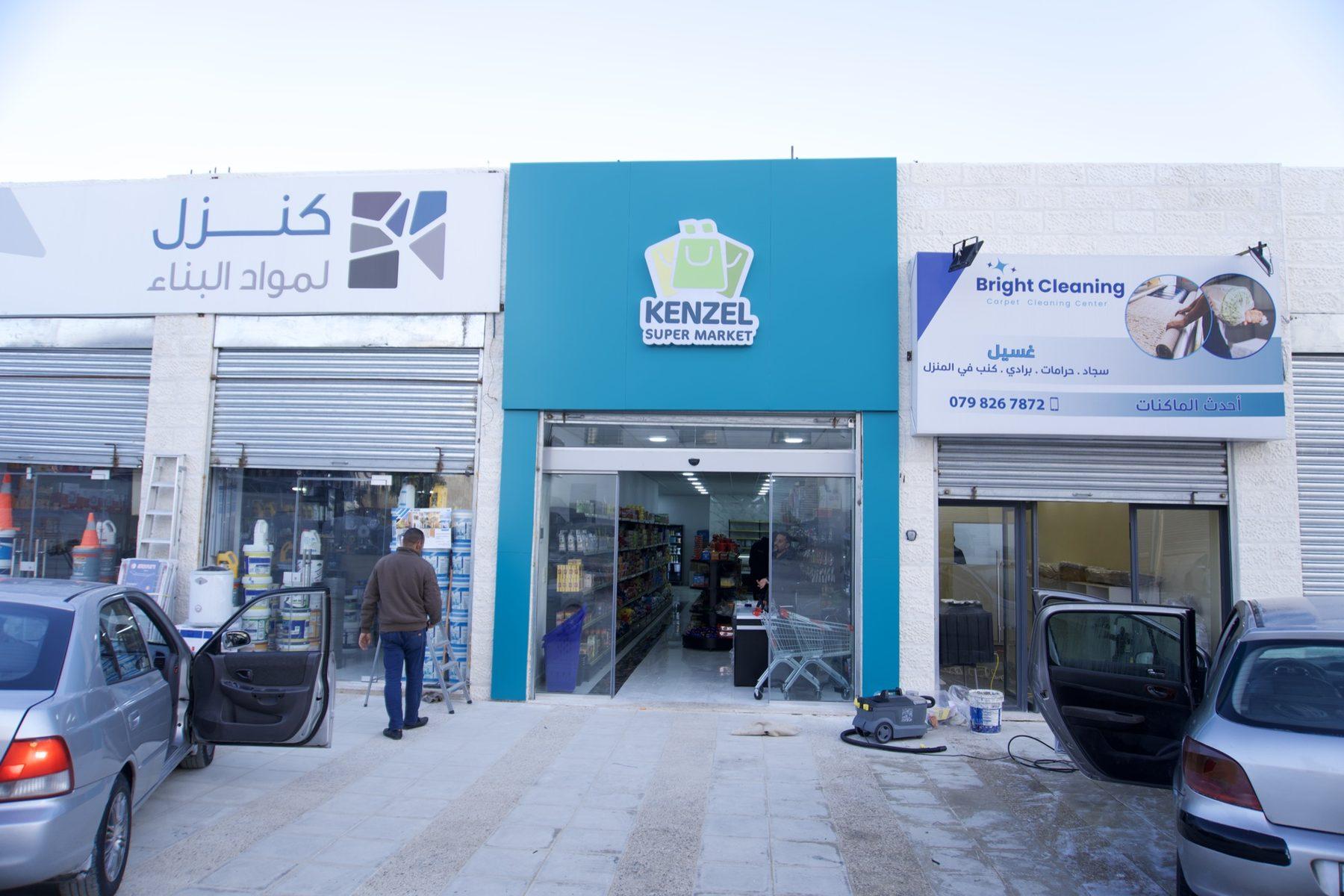 Storefront with a blue fascia sign above the entrance, with cars parked outside
