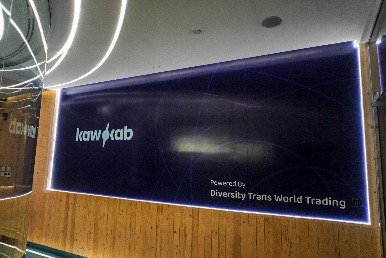 A backlit blue panel sign with a white logo over a timber wall.