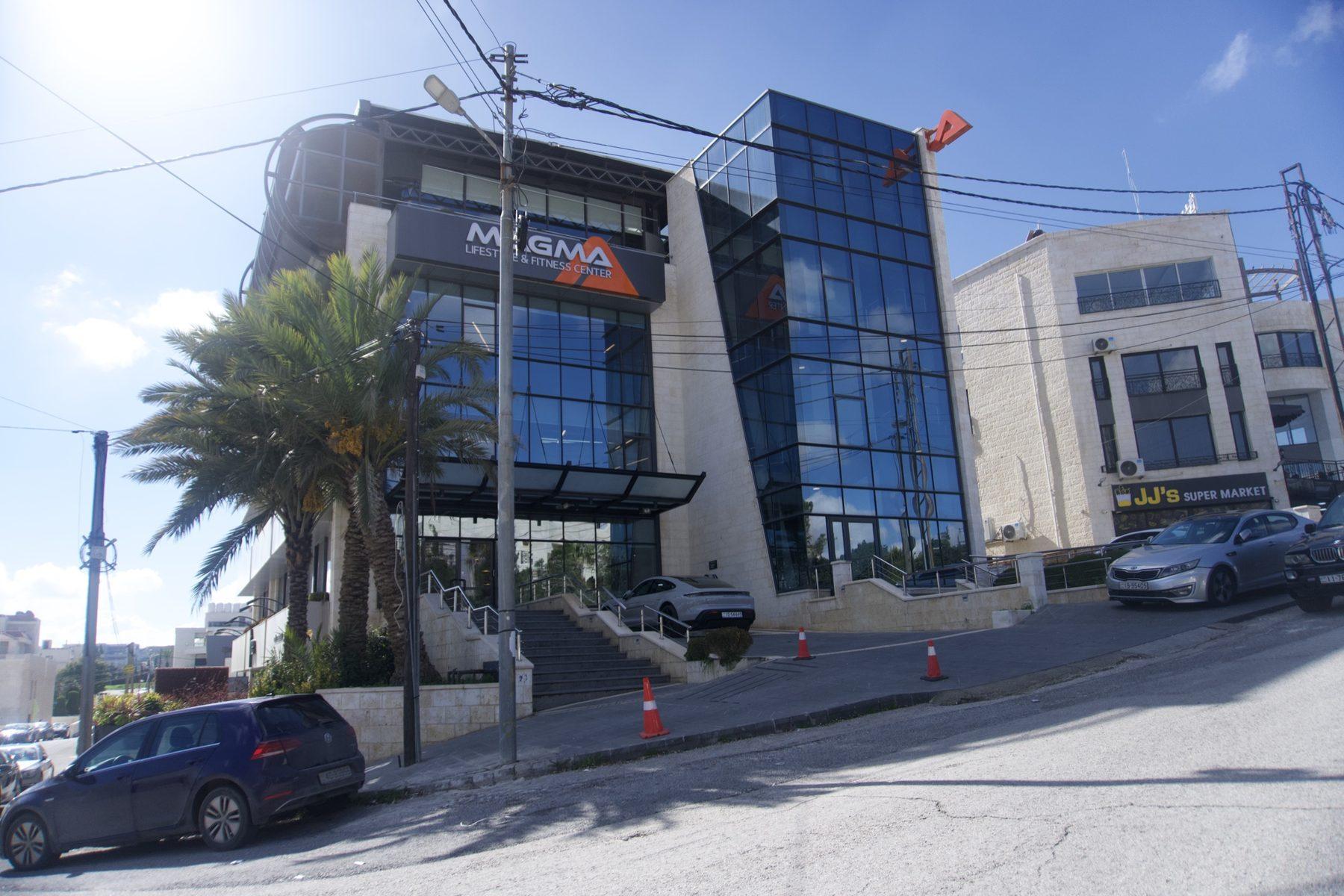 Logo fascia on a glass-fronted building with cars parked in front