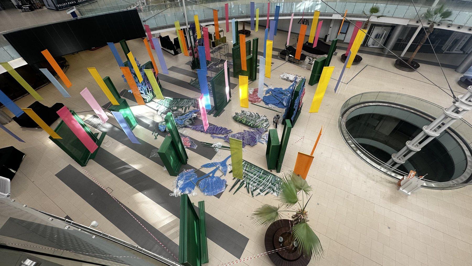 Overhead view of colourful tall panels arranged across the floor of a mall atrium.