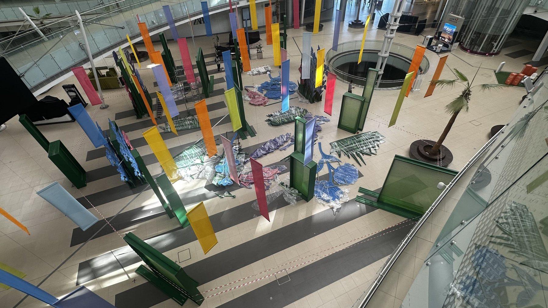 Wide overhead view of a mall atrium with colourful vertical panels and green pillars.