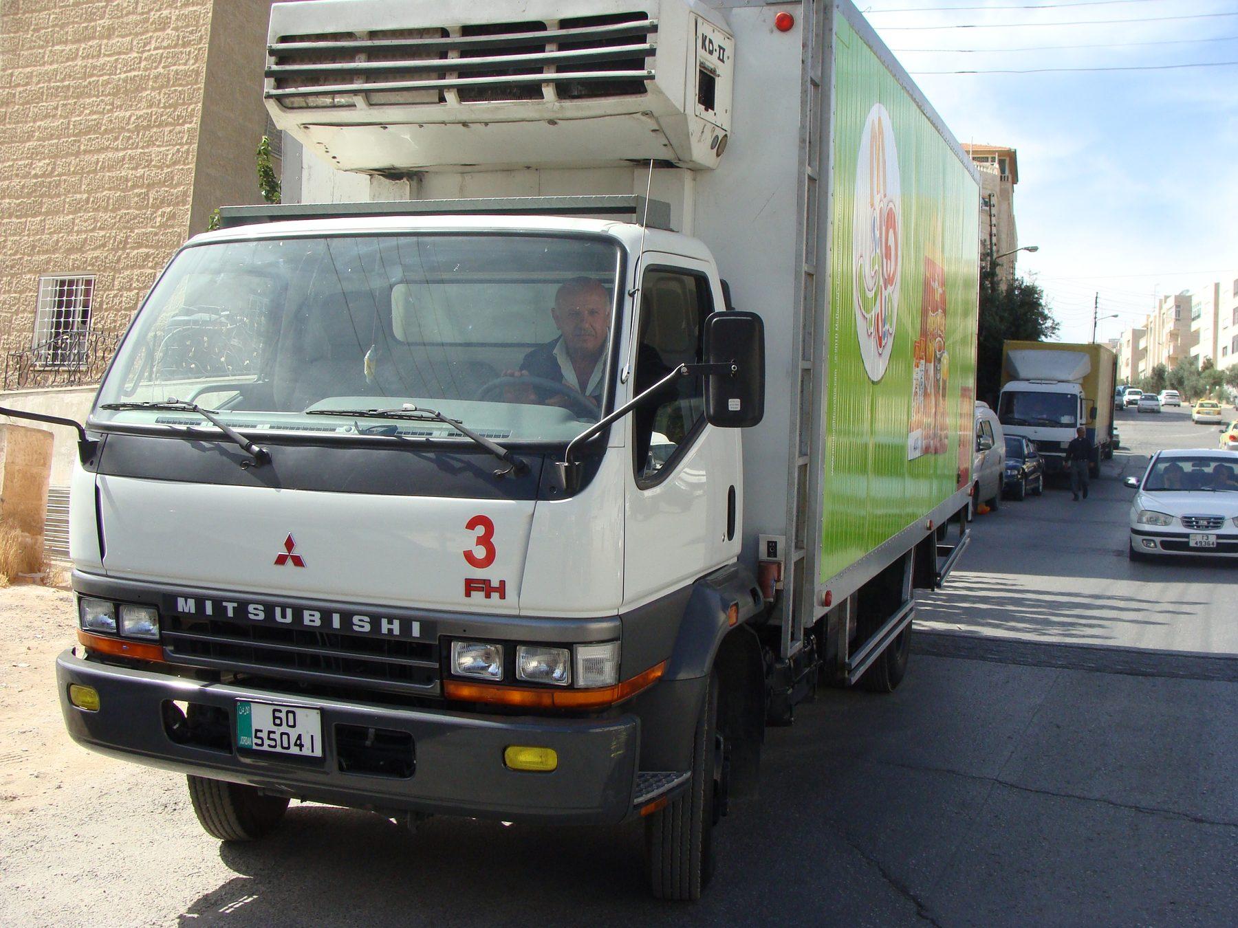 Front three-quarter view of a white truck with green box graphic