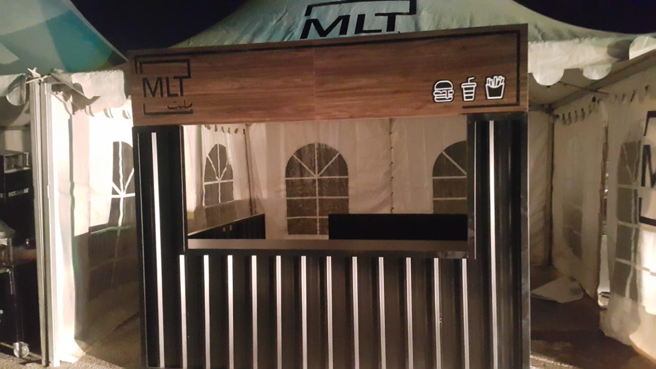 Wood-fronted counter booth with metal slats inside a white tent