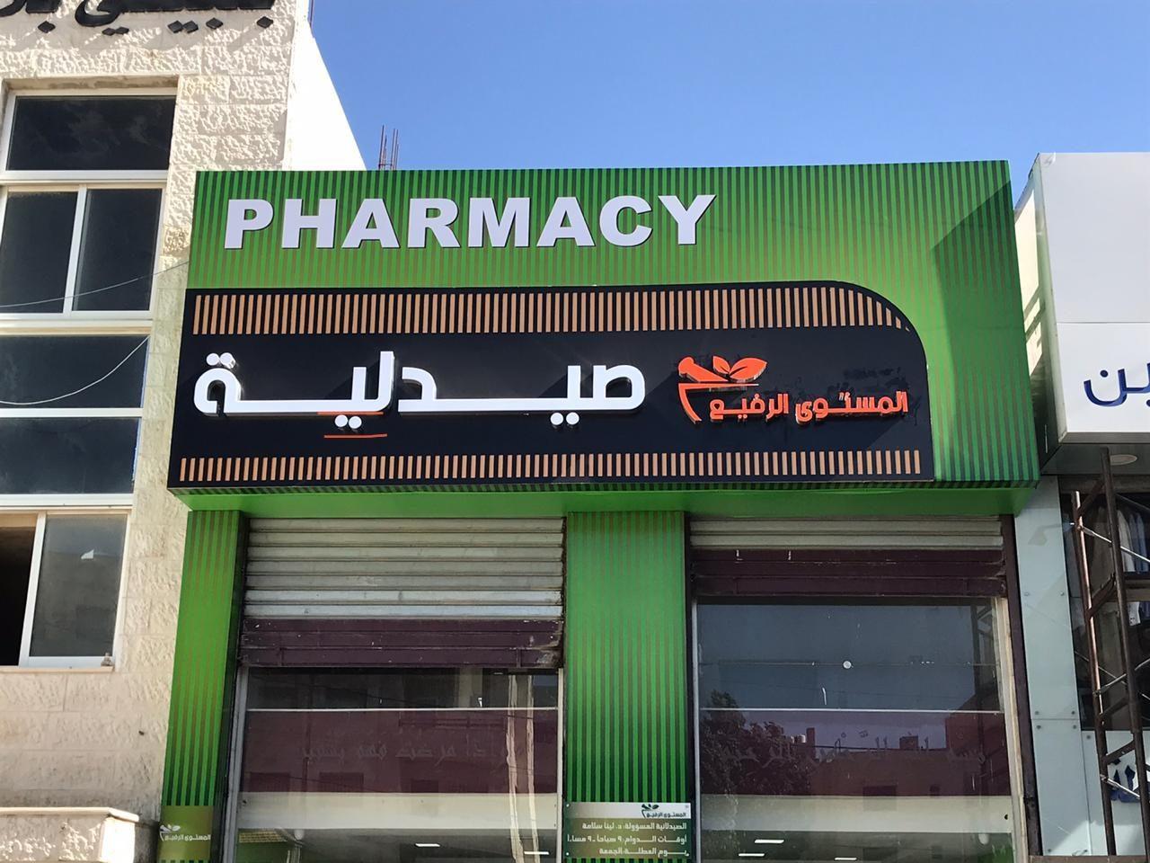 Green shopfront with a dark fascia sign in English and Arabic, in daylight