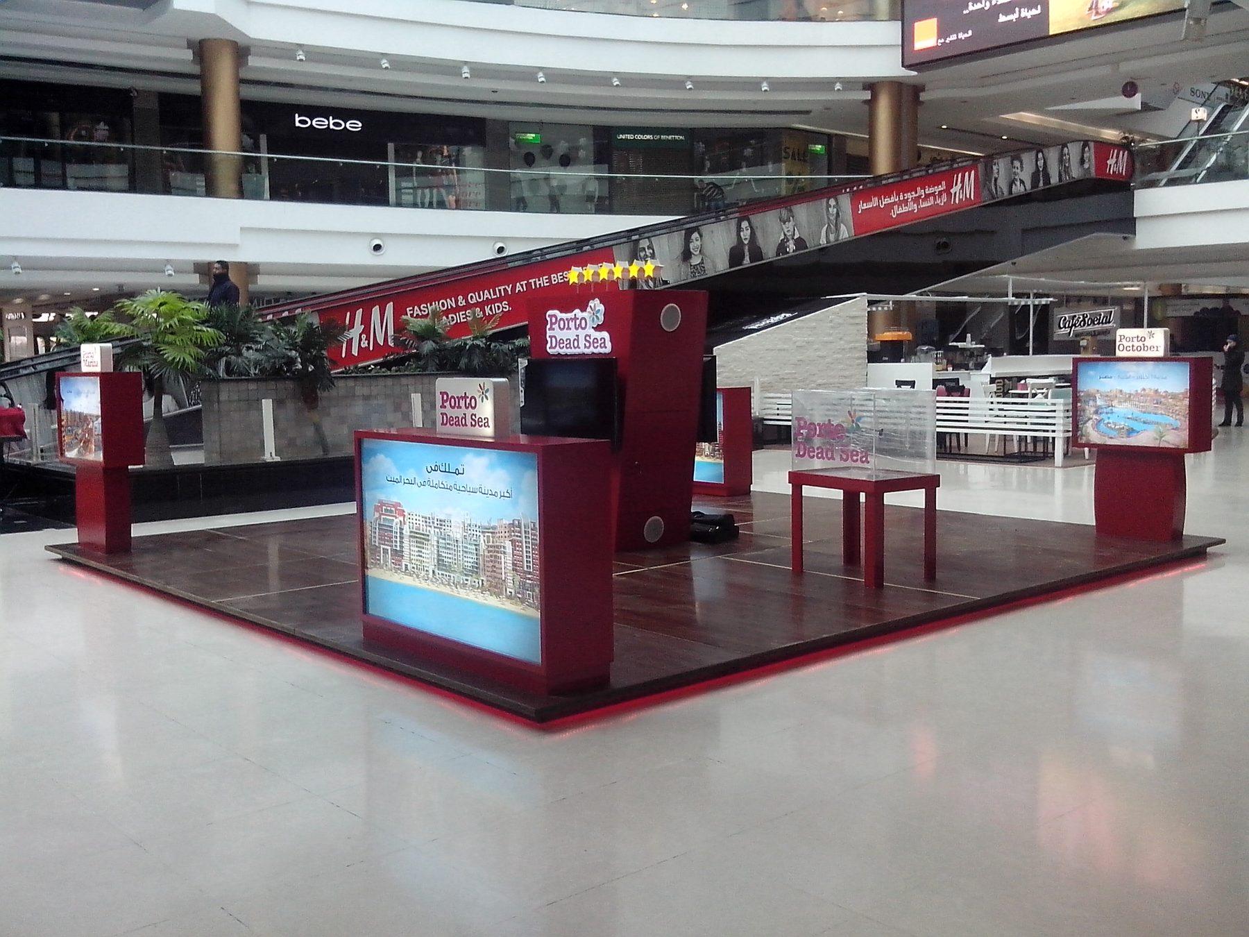 Red and white booth with two illuminated screens in a mall walkway