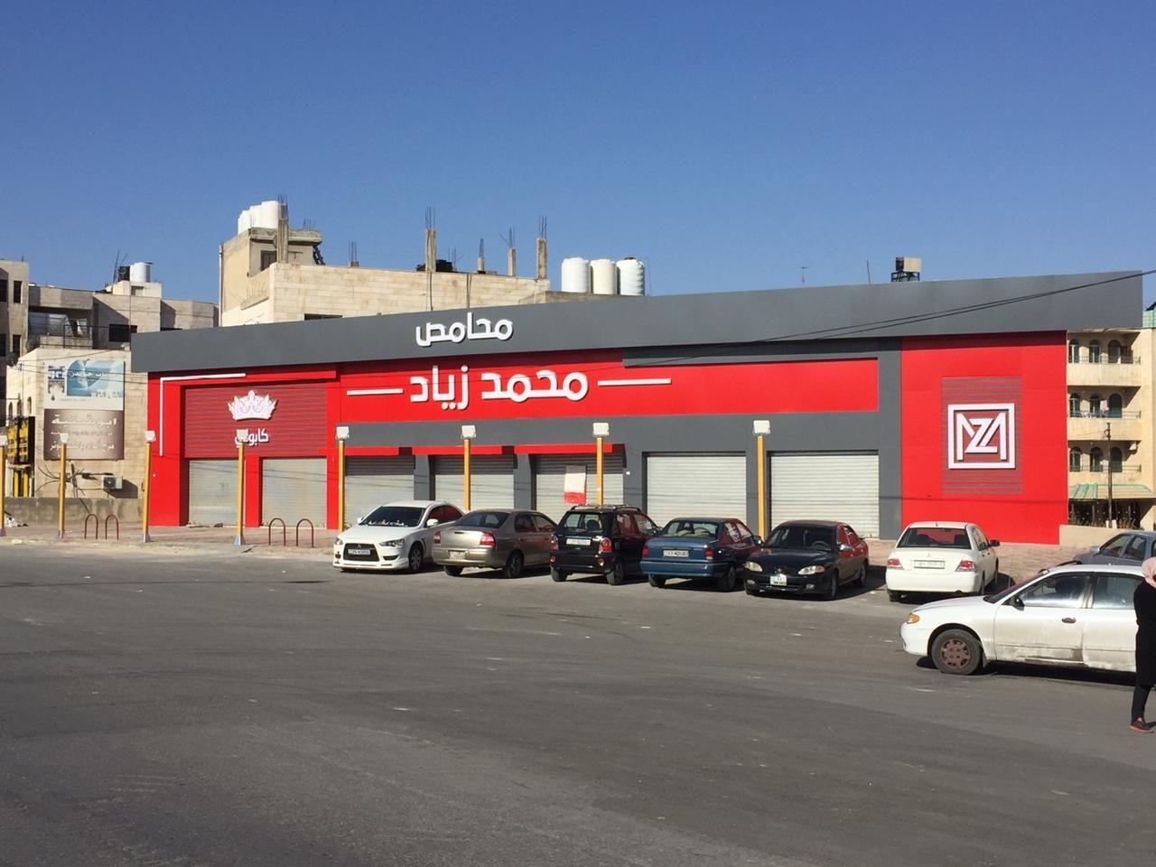 Red fascia band with Arabic lettering seen from across a car park