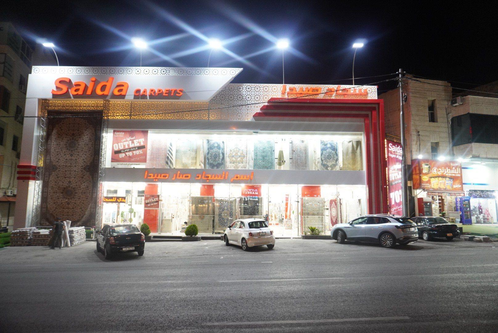 The front of a carpet showroom with an illuminated fascia sign at night.