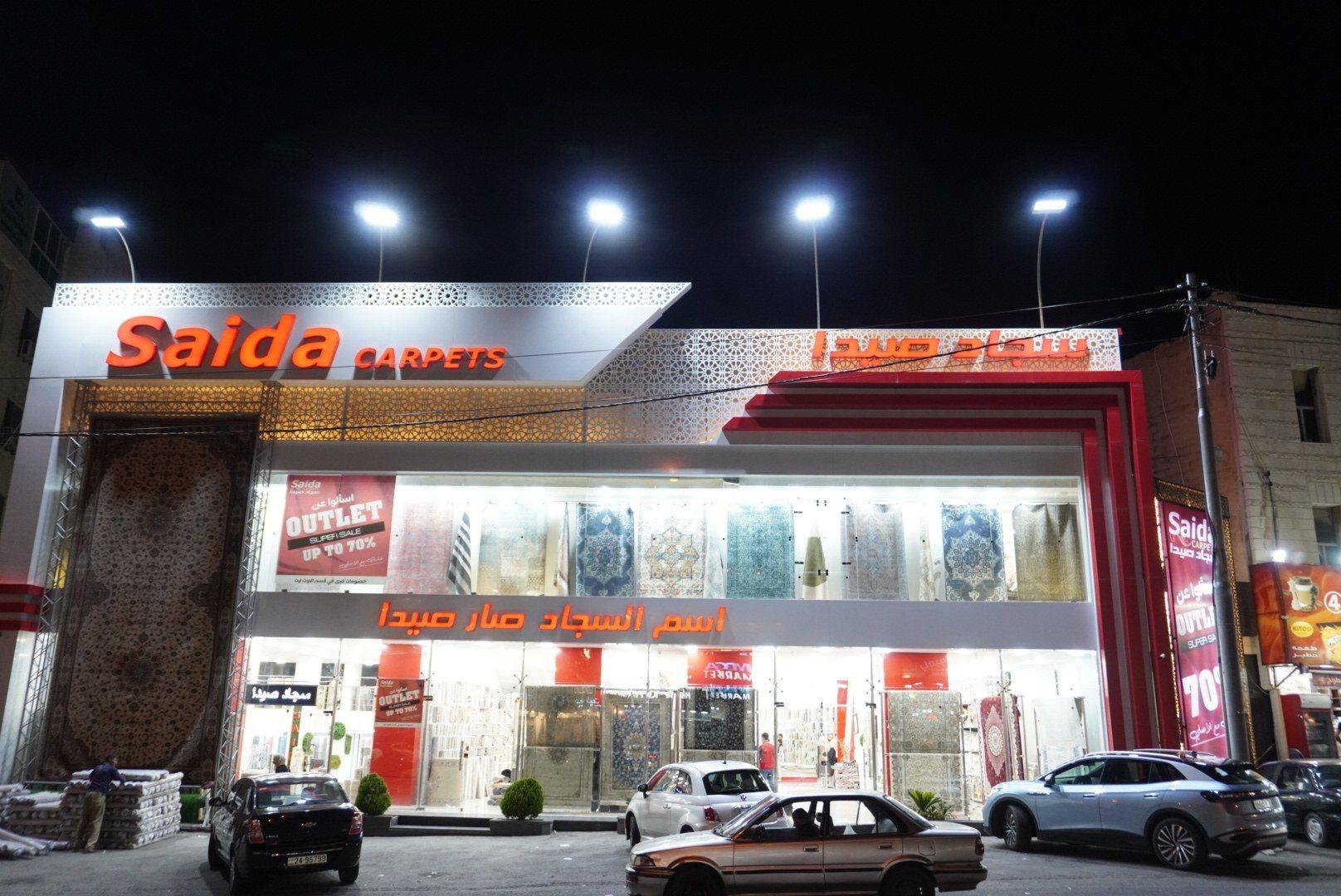 The front of a carpet showroom with an illuminated fascia sign at night.