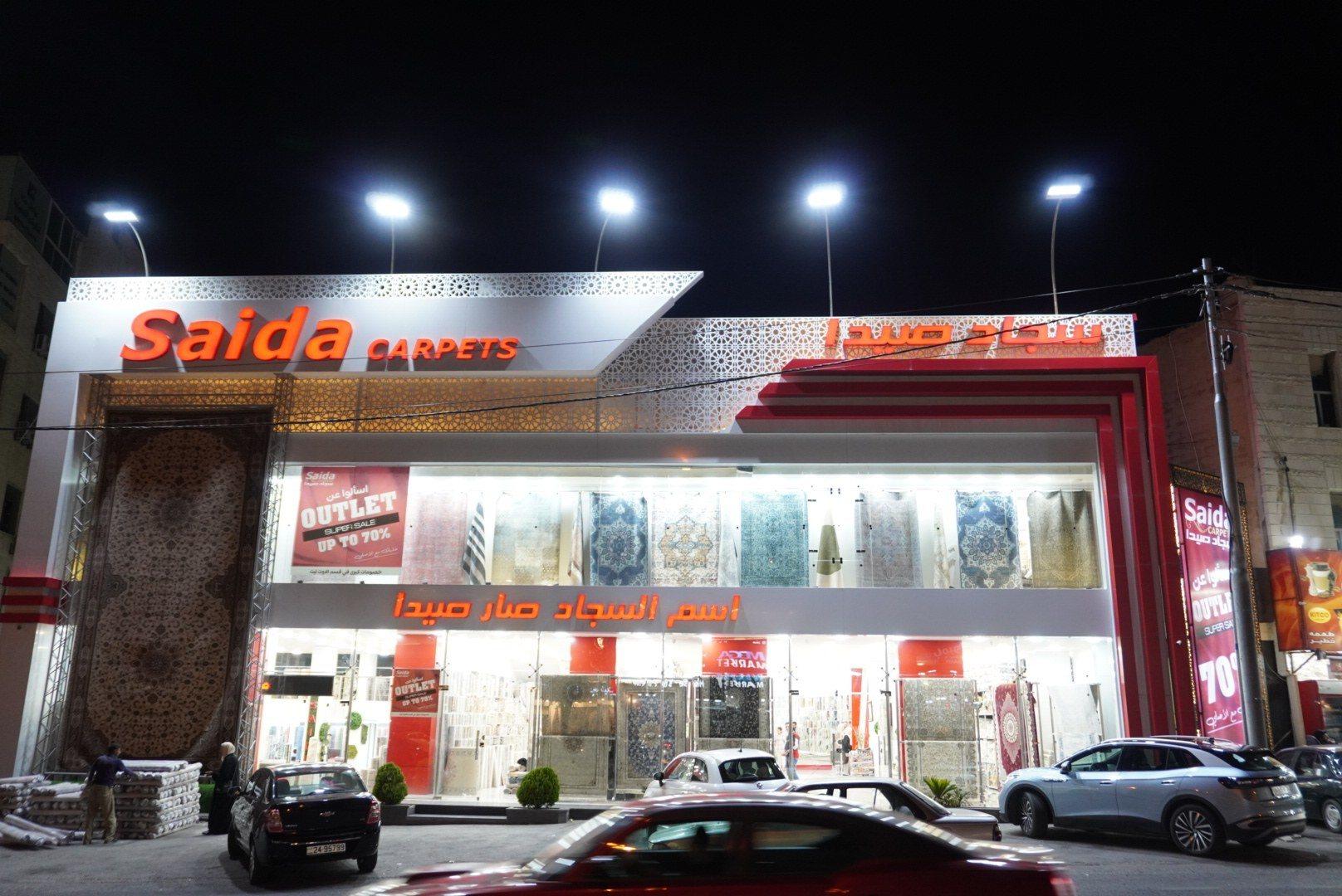 The front of a carpet showroom with an illuminated fascia sign at night.