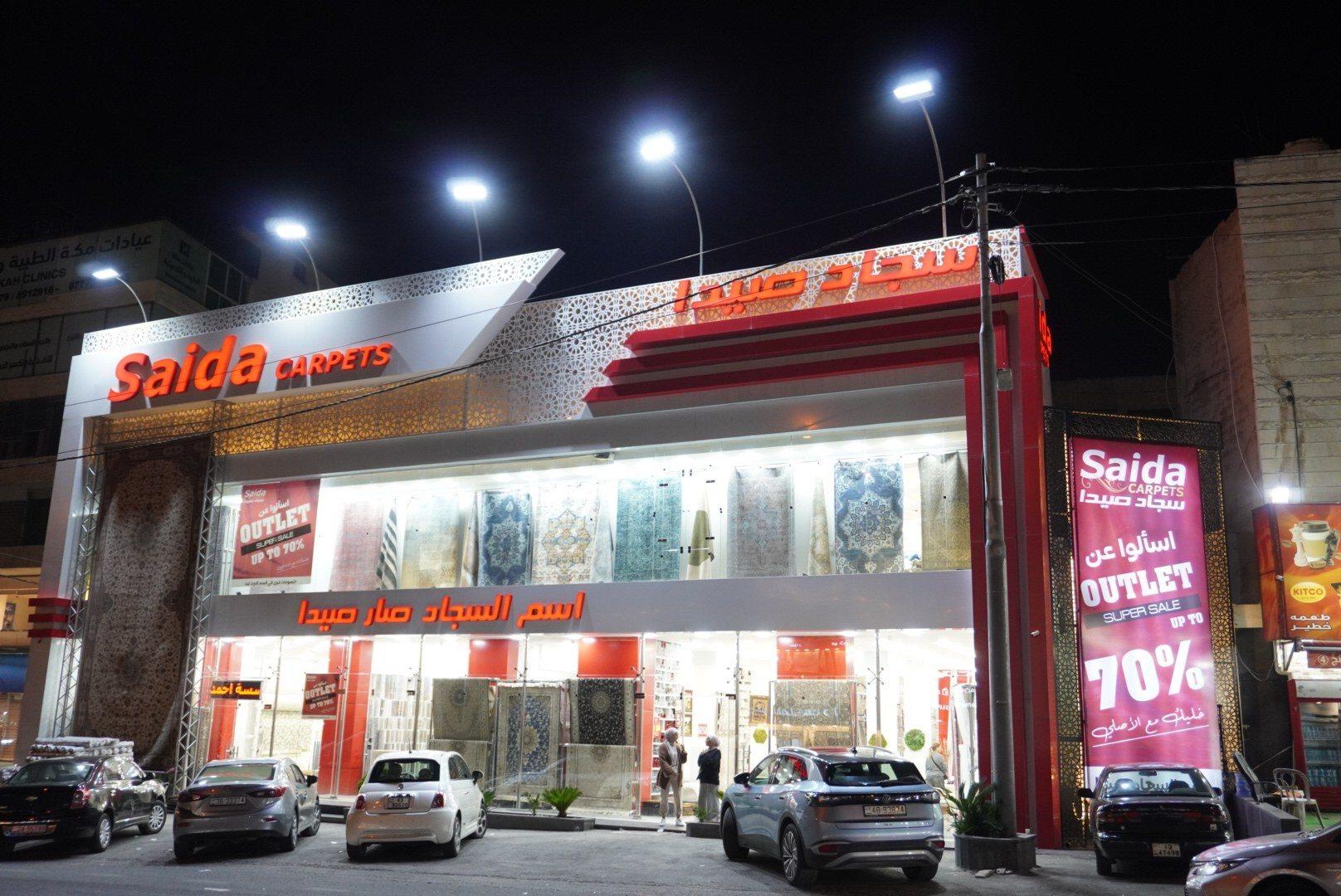 The front of a carpet showroom with an illuminated fascia sign at night.