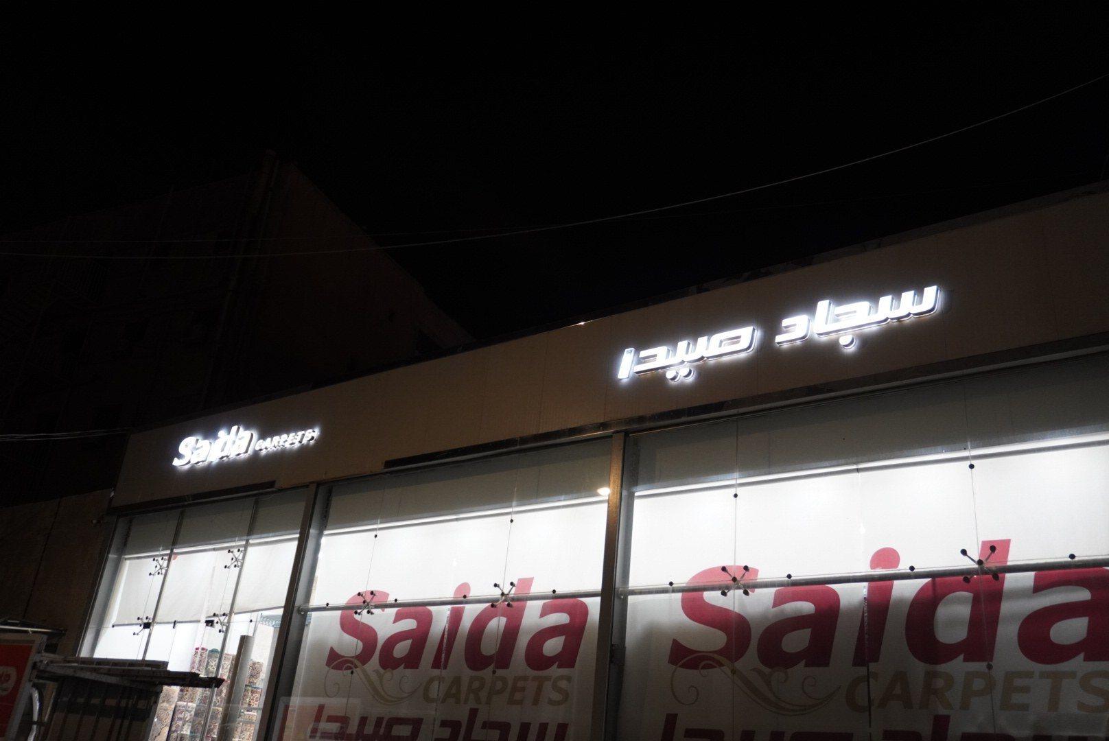 Illuminated lettering and window graphics on the facade of a carpet showroom at night.