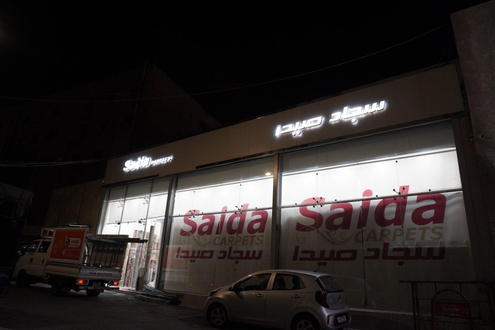 Illuminated lettering and window graphics on the facade of a carpet showroom at night.
