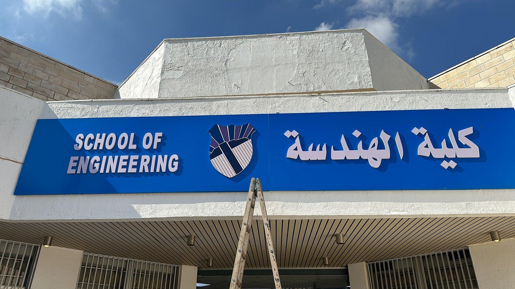 A blue fascia sign with English and Arabic lettering above a building entrance.