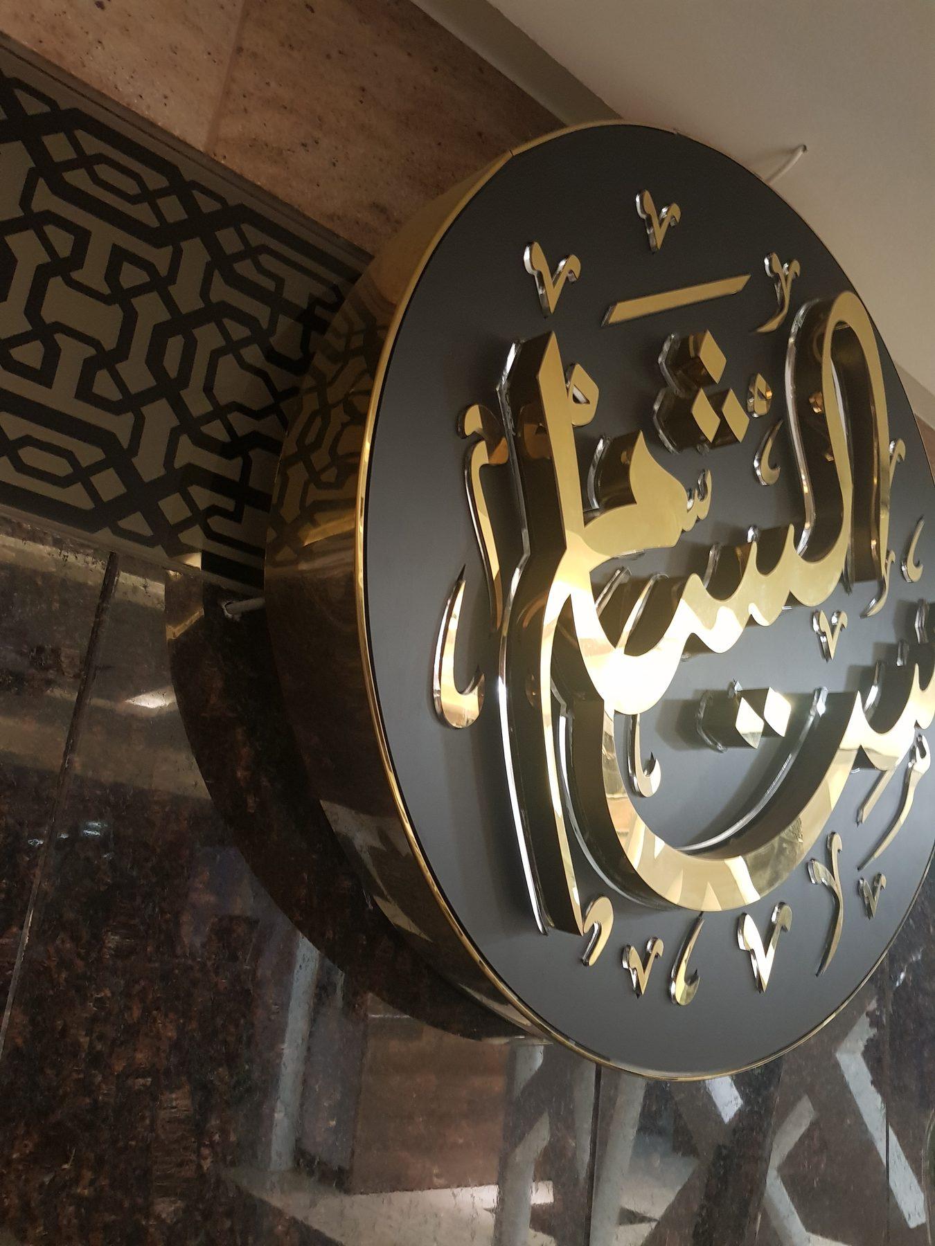 Close-up of the round black and gold sign with raised Arabic lettering