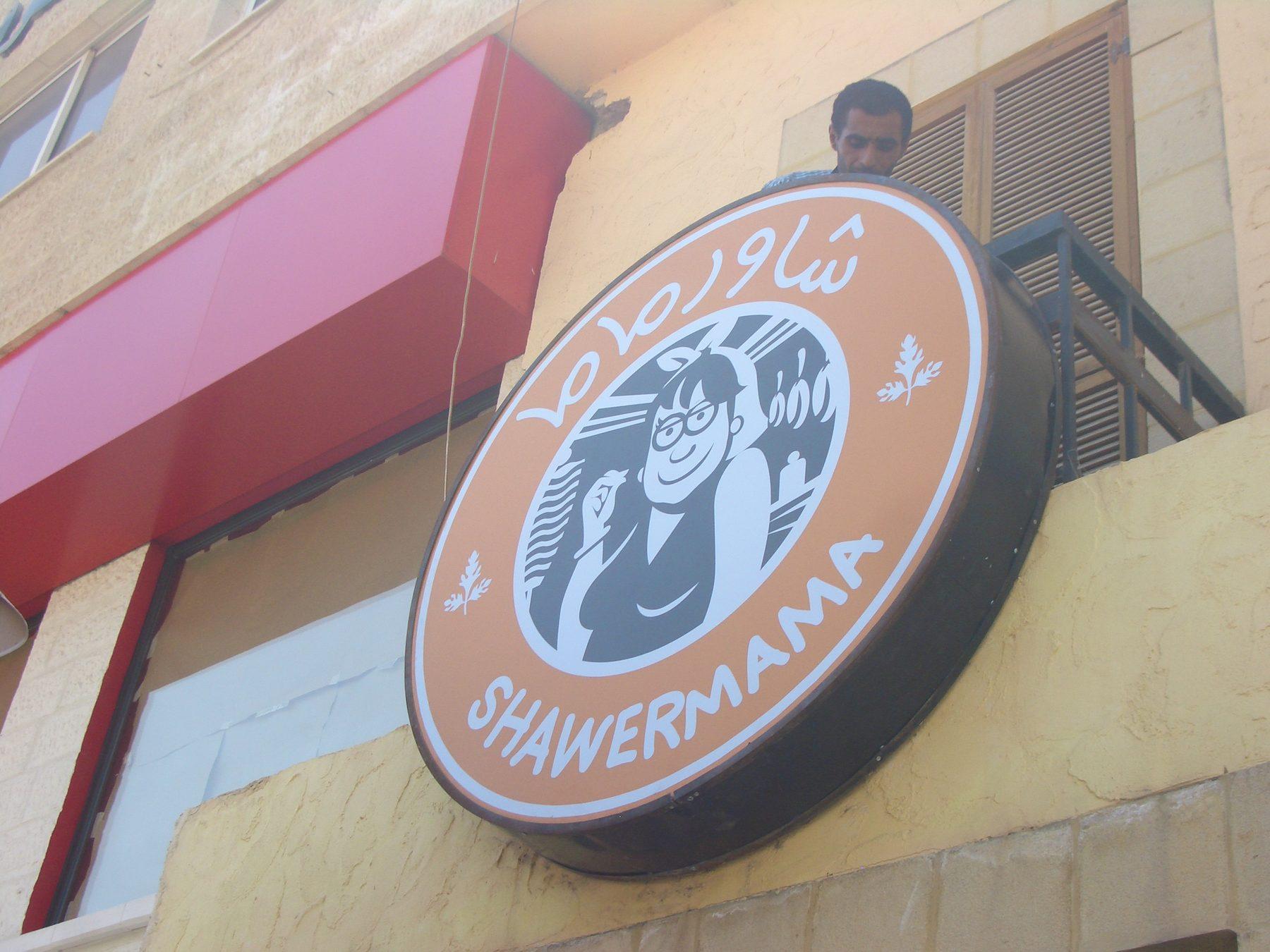 Round sign with chef illustration and name mounted on a building front
