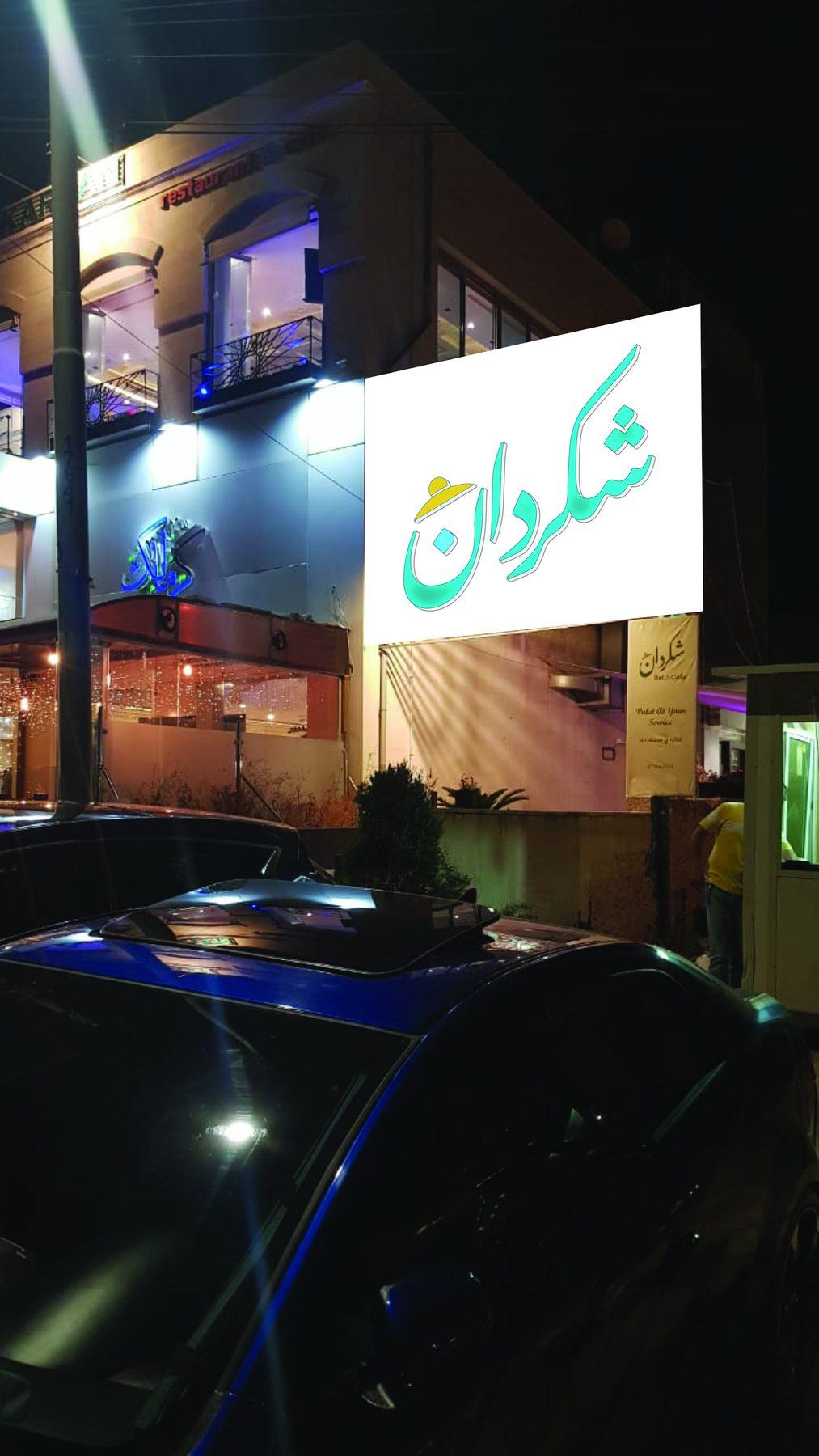 Illuminated white box sign with teal Arabic lettering projecting from the building at night.