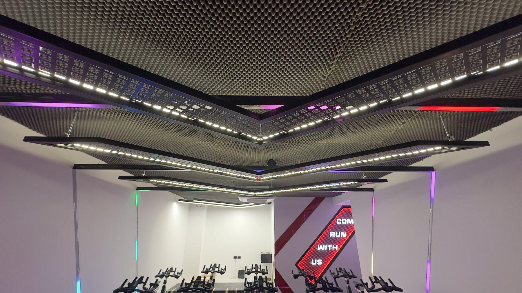 Perforated ceiling with linear LED strips and a red logo panel in a lit room.