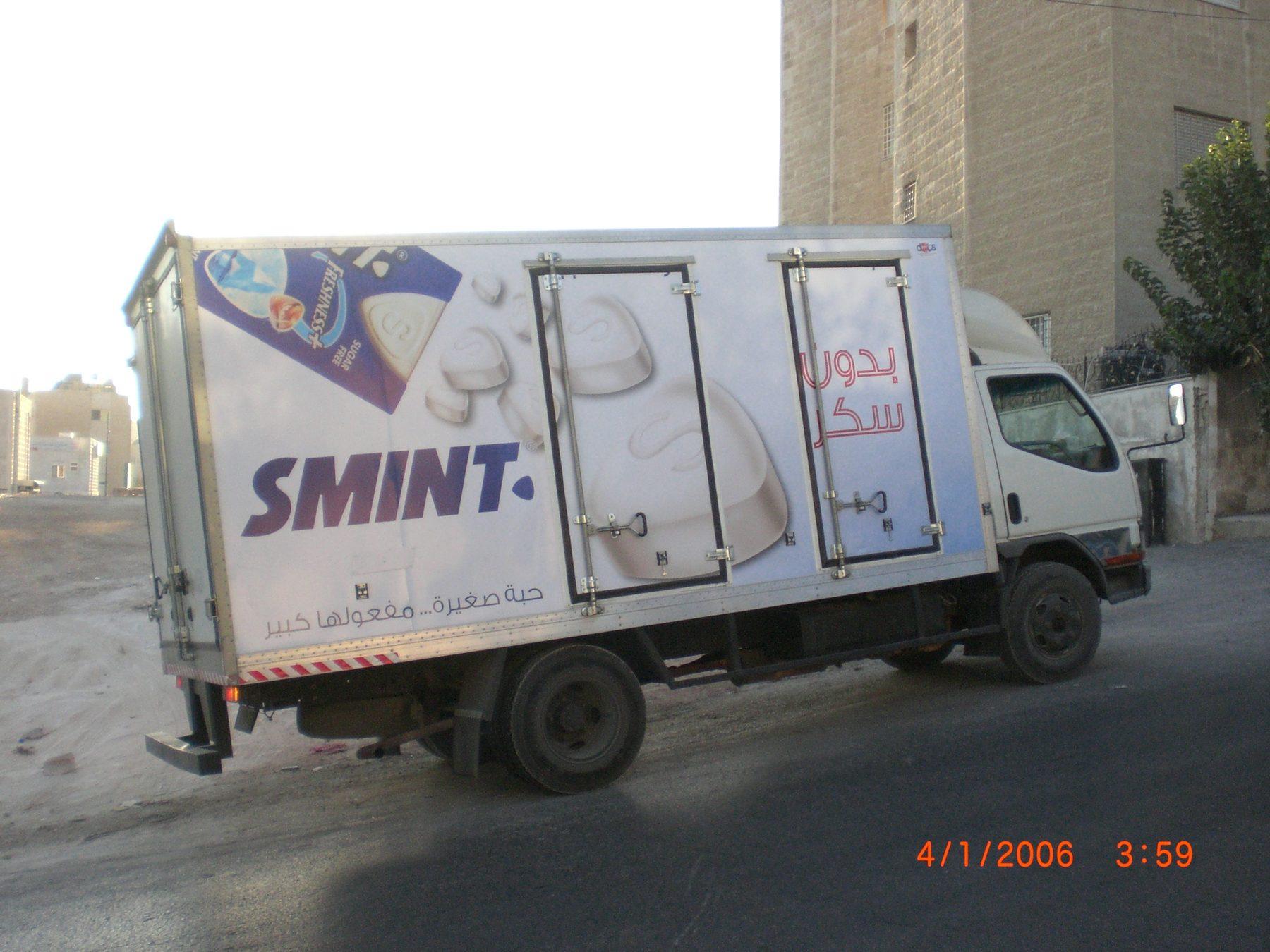 Side of a white box truck with gum product imagery and Arabic text.