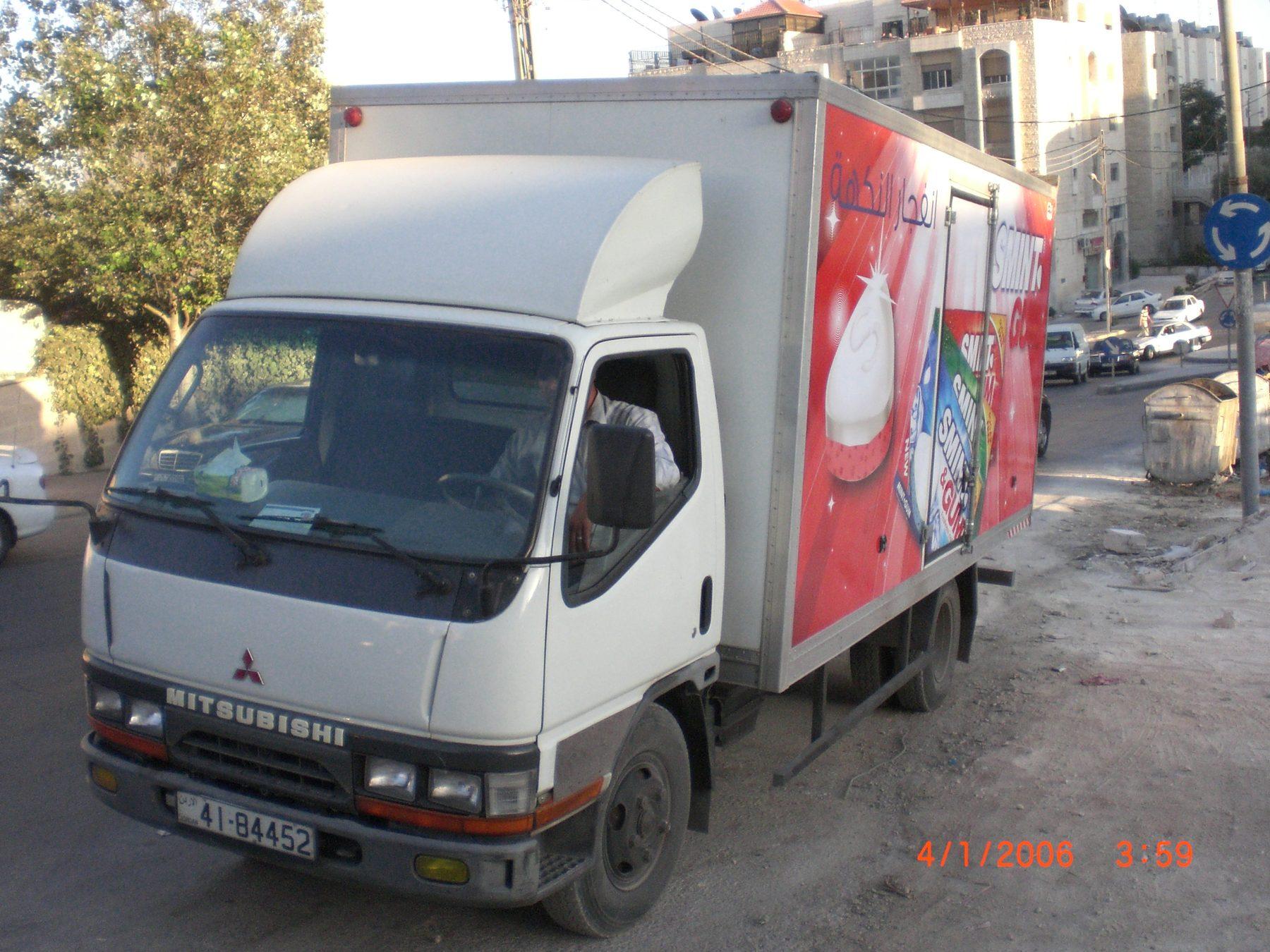 Front three-quarter view of a white truck with a red wrap on its box.