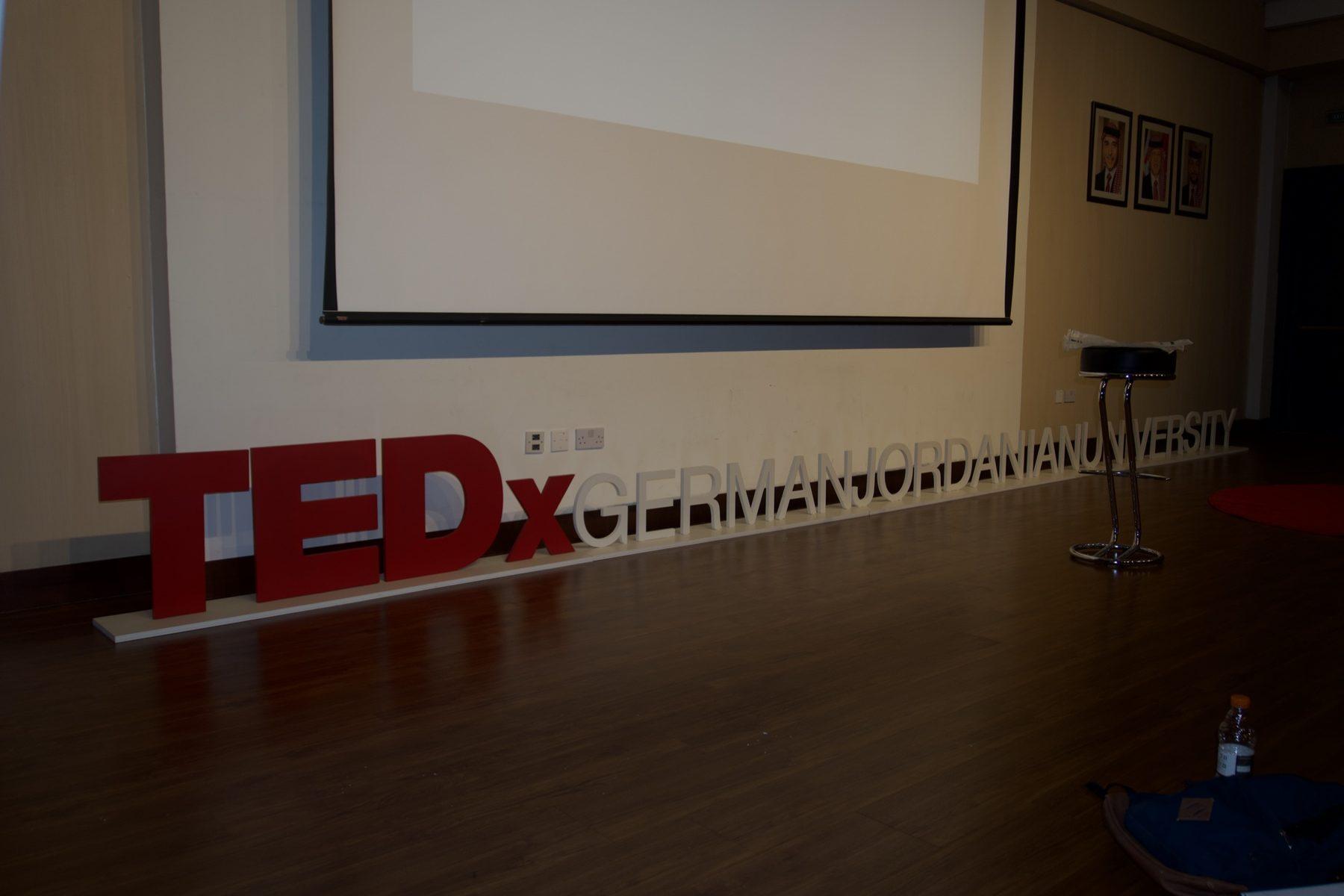 Red 3D letters on the stage floor in front of a projection screen and podium.