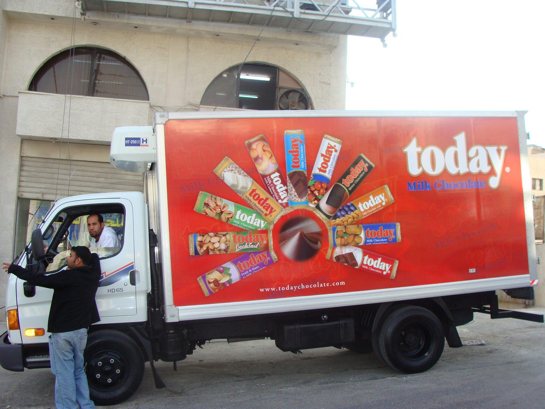 Red box truck with chocolate bar imagery, with a driver standing beside it.