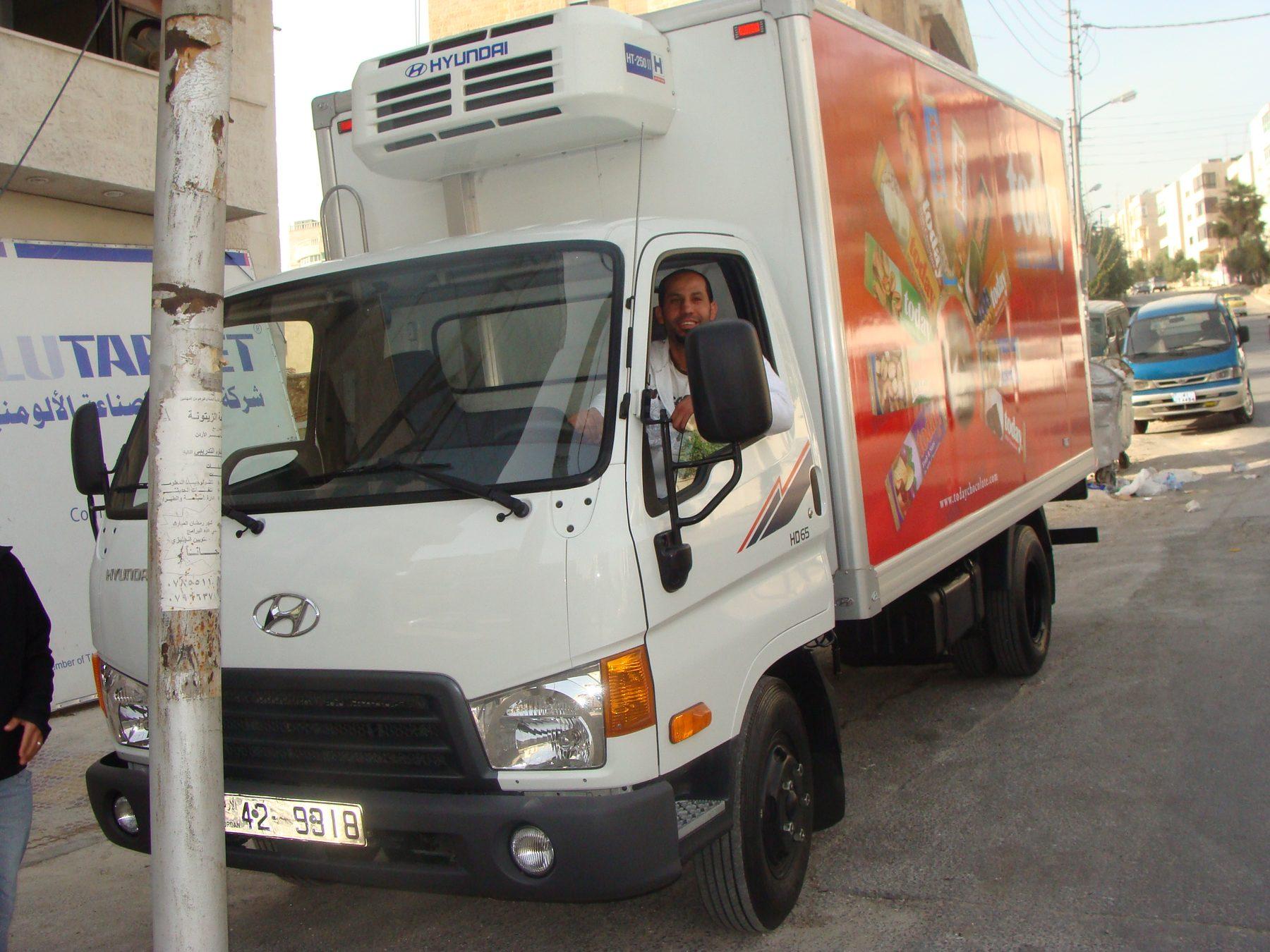 Front three-quarter view of a white truck with a red wrap on its box.