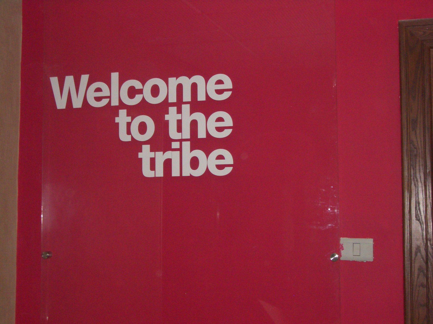Raised light-coloured lettering mounted on a red wall beside a wooden door.