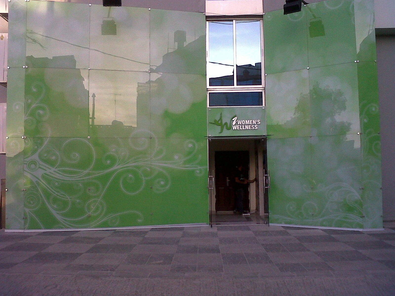 Green patterned glass wall with the entrance and a small logo at the door